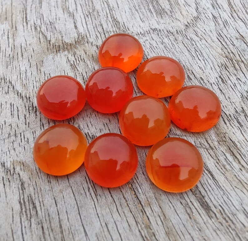 May include: Nine round, orange carnelian gemstones on a light wood surface.