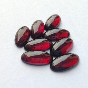 Peut inclure: Un groupe de dix pierres précieuses ovales de couleur rouge. Les pierres précieuses sont lisses et polies, d'une couleur rouge foncé.