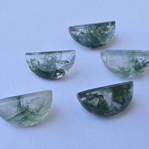 以下が含まれることがあります： 緑色の苔のような模様が内包された、半月型の宝石が5つ。透明感のある石が白い背景に配置され、内部の自然な模様が際立っています。それぞれの石は約1.5cmの直径です。