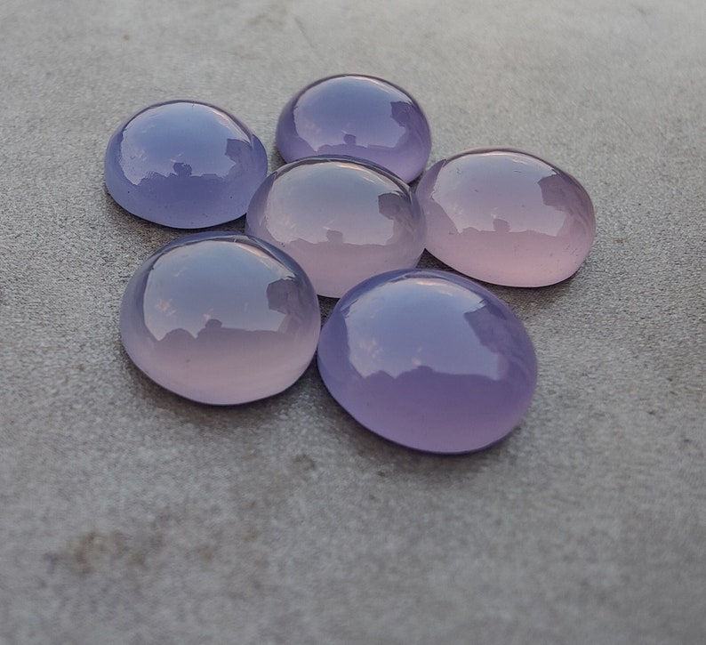 以下が含まれることがあります： 6つの丸い、滑らかで半透明の紫とピンクの宝石。石は灰色の表面に円形に配置されています。