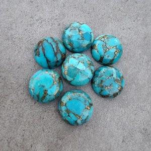 May include: Eight turquoise cabochons with gold flecks, arranged in a circle on a gray surface.