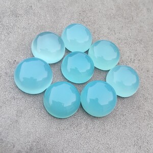 Pu&ograve; includere: Otto pietre preziose rotonde di cabochon blu chiaro disposte in cerchio su una superficie grigia.