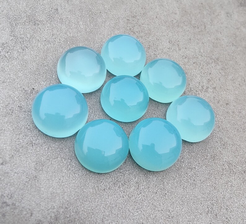 Pu&ograve; includere: Otto pietre preziose rotonde di cabochon blu chiaro disposte in cerchio su una superficie grigia.