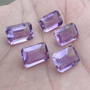 May include: Five faceted amethyst gemstones in a rectangular emerald cut. The gemstones are a light purple colour and have a smooth, polished finish.