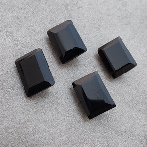 Pu&ograve; includere: Quattro cabochon rettangolari di pietra preziosa nera su uno sfondo grigio.