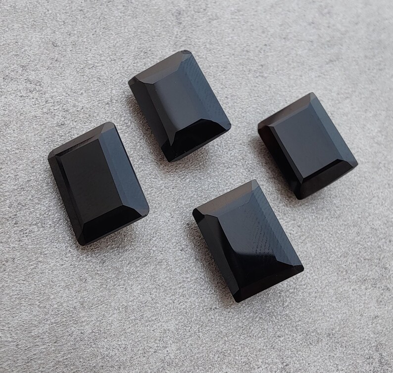 Pu&ograve; includere: Quattro cabochon rettangolari di pietra preziosa nera su uno sfondo grigio.