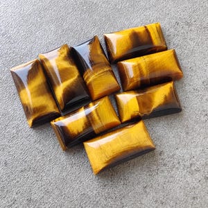 May include: A collection of eight rectangular tiger's eye gemstone cabochons in various shades of brown and gold.
