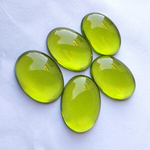 May include: Five oval-shaped, bright green glass cabochons. The cabochons are smooth and shiny.