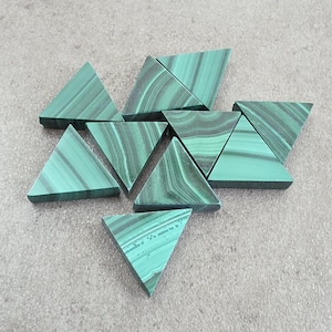 May include: A collection of eight triangular-shaped malachite pieces, each featuring distinct dark and light green banded patterns. The stones are arranged in a loose cluster, showcasing the natural, swirling mineral striations on their flat surfaces.