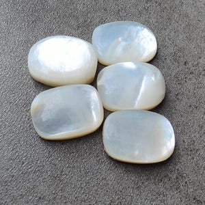 Könnte beinhalten: Fünf weiße, ovale Perlmuttsteine. Die Steine sind glatt und haben einen Perlmuttglanz.