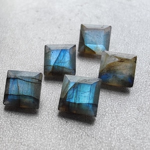 May include: Five square-shaped labradorite gemstones with iridescent blue and grey hues.