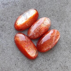 K&ouml;nnte beinhalten: Vier ovale Sonnenstein-Cabochons in rot-orange mit schimmerndem, irisierendem Finish.