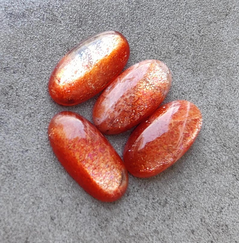 K&ouml;nnte beinhalten: Vier ovale Sonnenstein-Cabochons in rot-orange mit schimmerndem, irisierendem Finish.