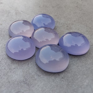以下が含まれることがあります： 薄いピンクがかったラベンダー色の滑らかで丸いカルセドニーのカボションが6つ。カボションはグレーの表面に集まって配置されています。