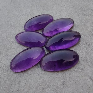 Könnte beinhalten: Sechs ovale Amethyst-Edelsteine, jeder mit einem tiefen violetten Farbton und einer glatten, polierten Oberfläche.