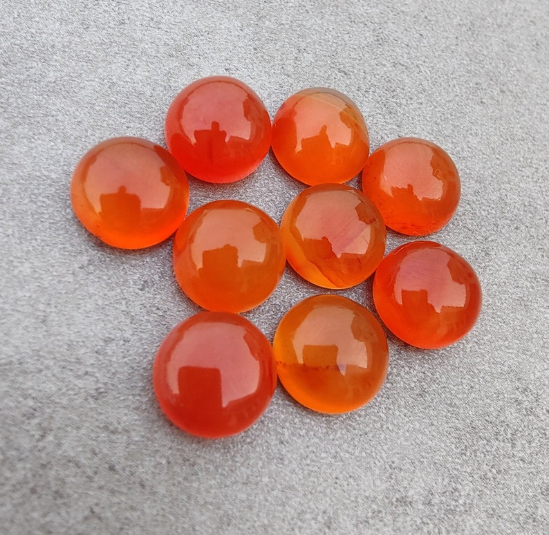 May include: Ten round, orange carnelian gemstones. The gemstones are smooth and polished.
