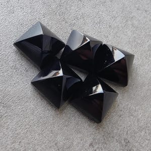 Könnte beinhalten: Fünf schwarze pyramidenförmige Edelsteine, wahrscheinlich Obsidian, auf einer grauen Oberfläche angeordnet.