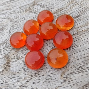 May include: Nine round, orange carnelian gemstones. The stones are smooth and polished, with a slight variation in color.