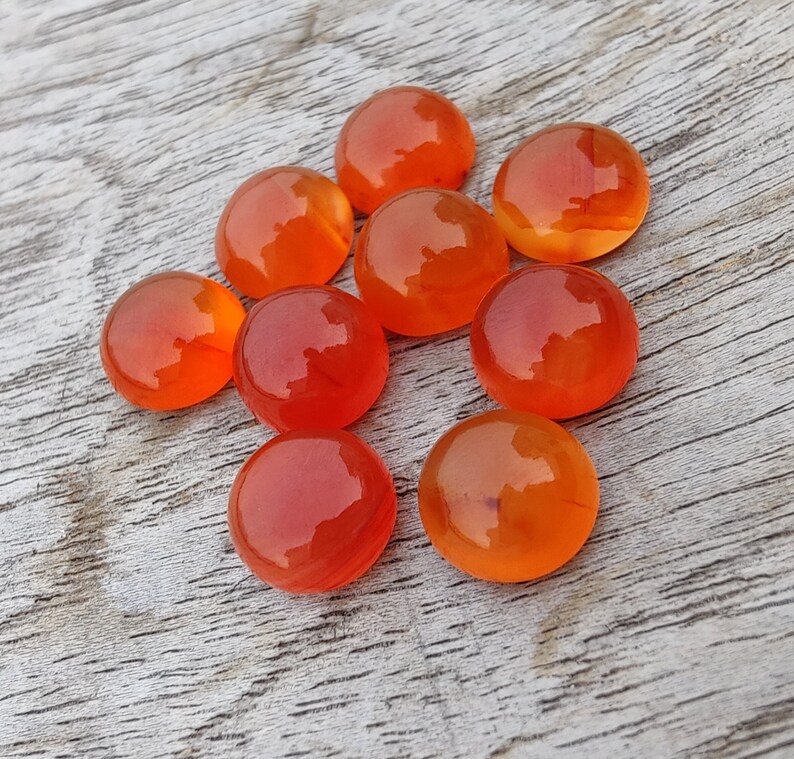 May include: Nine round, orange carnelian gemstones. The stones are smooth and polished, with a slight variation in color.