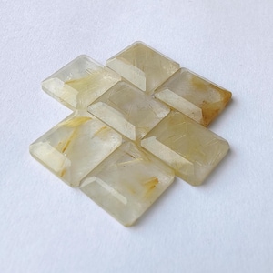 Puede incluir: Siete gemas rectangulares facetadas con un tono amarillo claro e inclusiones doradas internas. Las gemas están dispuestas en un patrón ligeramente superpuesto sobre un fondo blanco, mostrando su claridad y corte.