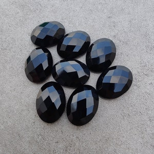 Puede incluir: Ocho piedras preciosas ovaladas negras con corte facetado. Las piedras preciosas están dispuestas en un racimo sobre una superficie gris.