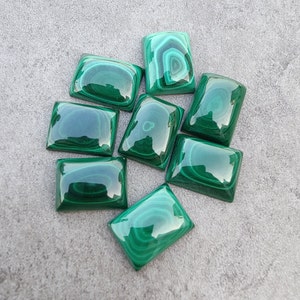 Puede incluir: Una colección de ocho cabujones de malaquita verde, cada uno con un patrón único de vetas verdes y blancas que se arremolinan. Los cabujones son lisos y pulidos, y tienen una apariencia ligeramente translúcida.