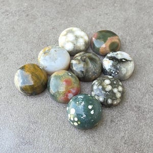 May include: A collection of ten polished gemstone spheres in various colors, including green, brown, white, and red. The spheres are arranged on a gray surface, showcasing their unique patterns and textures. These decorative stones are ideal for collectors.