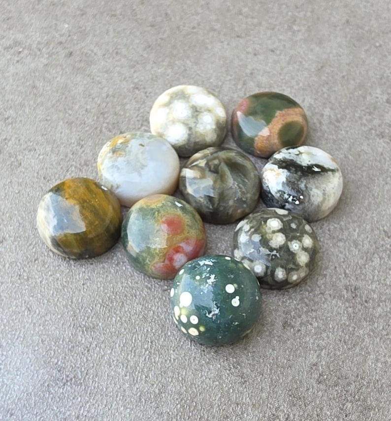 May include: A collection of ten polished gemstone spheres in various colors, including green, brown, white, and red. The spheres are arranged on a gray surface, showcasing their unique patterns and textures. These decorative stones are ideal for collectors.