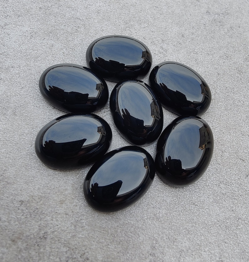 May include: Seven smooth, oval-shaped black gemstones. The stones are polished and have a glossy finish.
