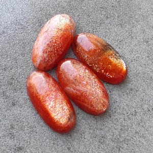 K&ouml;nnte beinhalten: Vier ovale Cabochons aus Sunstone mit schimmerndem, irisierendem Finish. Die Steine sind eine Mischung aus Orange, Rot und Gold.