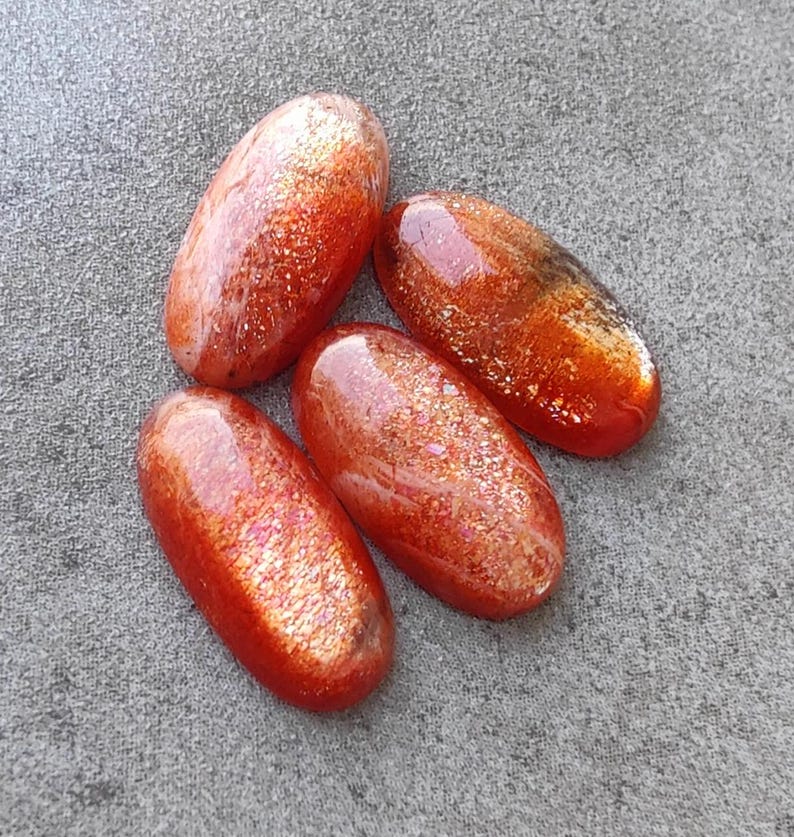 K&ouml;nnte beinhalten: Vier ovale Cabochons aus Sunstone mit schimmerndem, irisierendem Finish. Die Steine sind eine Mischung aus Orange, Rot und Gold.
