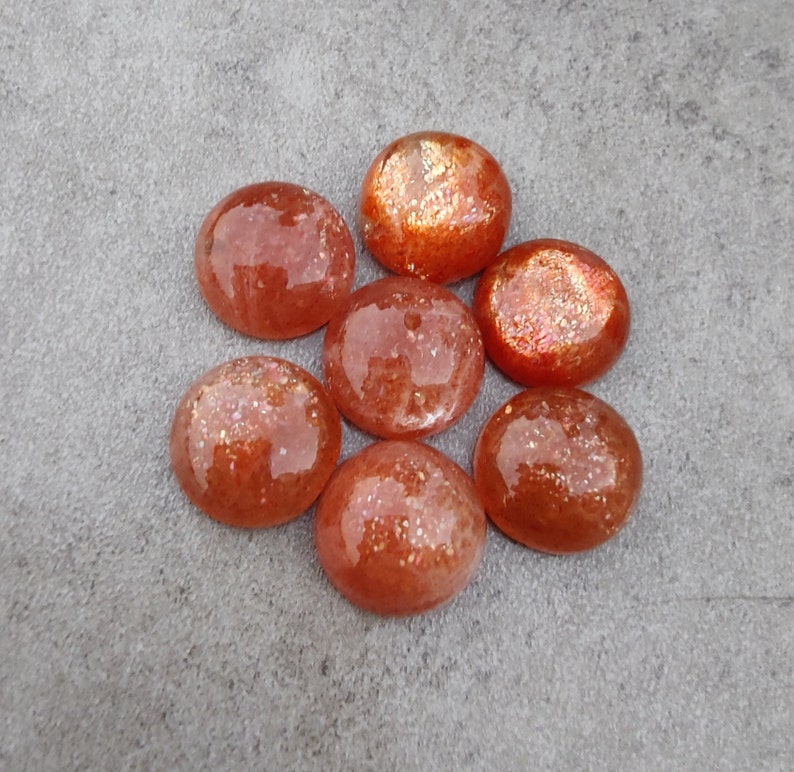 May include: Seven round, orange sunstone cabochons with a sparkly, iridescent finish.