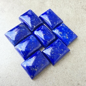 May include: Nine polished, rectangular lapis lazuli gemstones. The deep blue stones have a glossy finish and are flecked with small, golden pyrite inclusions. The gemstones are arranged in a diamond shape.