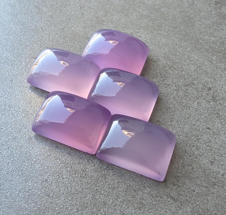 Pu&ograve; includere: Cinque pietre preziose rettangolari lucide in varie tonalit&agrave; di lavanda e viola. Le pietre hanno una parte superiore arrotondata e una finitura lucida, che riflette la luce. Le pietre sono disposte in modo leggermente sovrapposto.