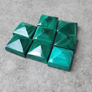 May include: Nine square malachite stones, each cut into a pyramid shape. The stones are a vivid green with darker green veining. They are arranged on a grey surface.