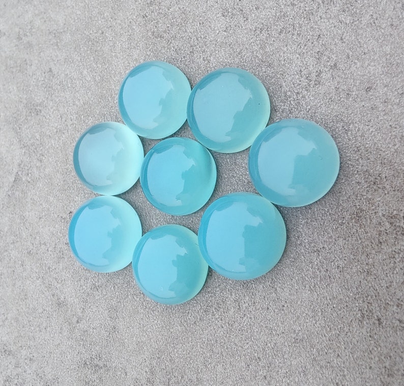 Pu&ograve; includere: Otto pietre preziose rotonde, lisce e di colore blu chiaro. Le pietre preziose sono disposte in cerchio su una superficie grigia.