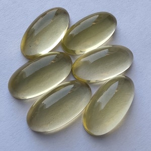 May include: Six oval-shaped, translucent, light yellow gemstones. The gemstones are smooth and polished.