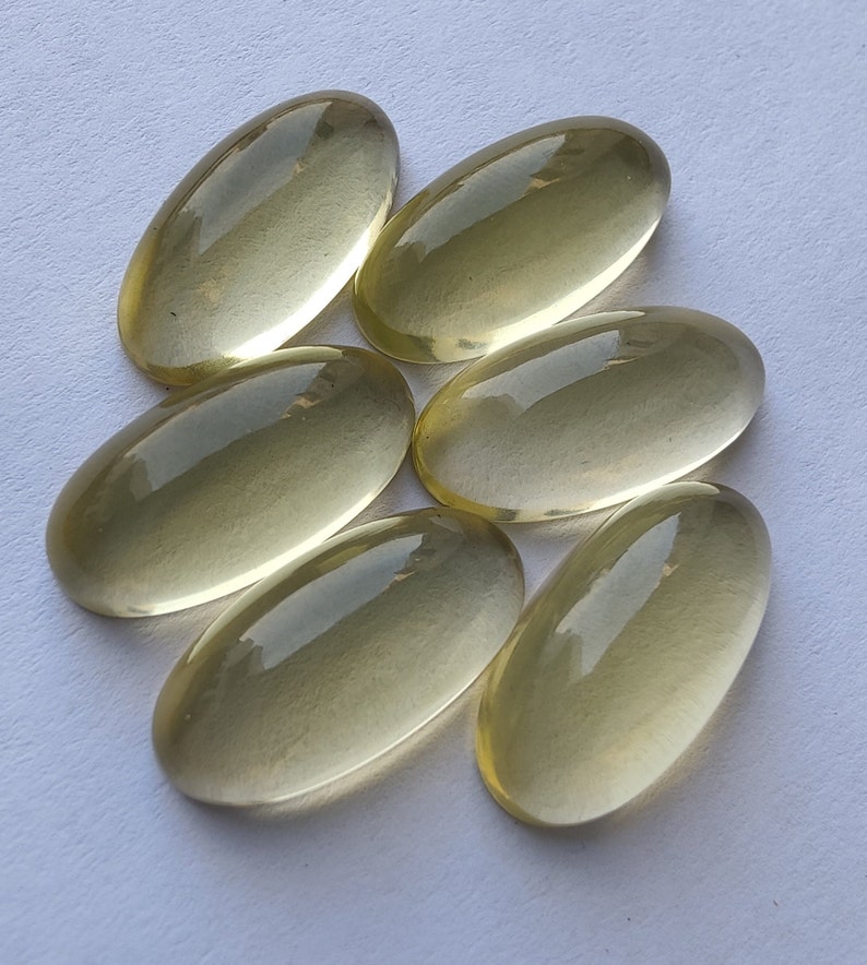 May include: Six oval-shaped, translucent, light yellow gemstones. The gemstones are smooth and polished.