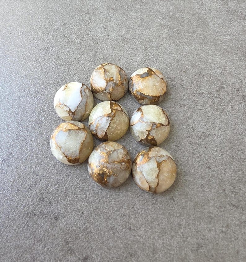 May include: Nine round, polished stones with a cream and gold color scheme. The stones have a marbled appearance with gold veining throughout. The stones are arranged in a square pattern on a gray surface.