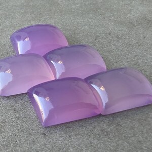 Pu&ograve; includere: Cinque gemme lucidate, a taglio quadrato, in varie tonalit&agrave; di lavanda e viola. Le pietre sono disposte in modo leggermente sovrapposto, con una superficie lucida e riflettente. Le gemme sono su uno sfondo grigio neutro.