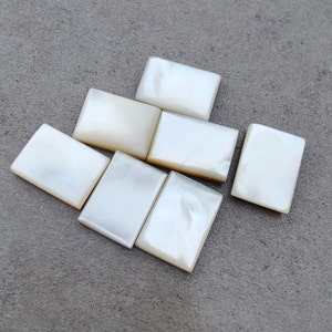 May include: Seven rectangular white mother-of-pearl tiles, arranged in a staggered pattern on a grey surface.