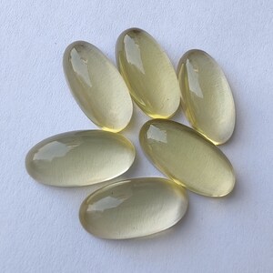 May include: Six oval-shaped, translucent, light yellow gemstones. The gemstones are smooth and polished.