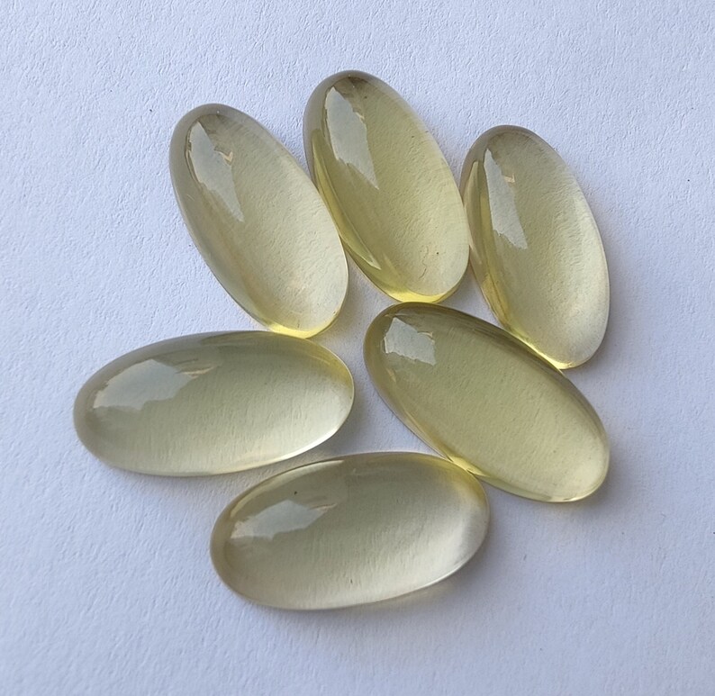 May include: Six oval-shaped, translucent, light yellow gemstones. The gemstones are smooth and polished.