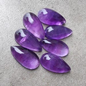 Op de afbeelding: Een groep van zeven paarse amethist edelsteen cabochons in een traanvorm.