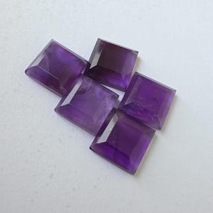 Peut inclure: Cinq pierres pr&eacute;cieuses d'am&eacute;thyste taill&eacute;es en carr&eacute;, de diff&eacute;rentes nuances de violet, sont dispos&eacute;es sur une surface blanche. Les pierres ont un design &agrave; facettes, captant la lumi&egrave;re et mettant en valeur leur couleur riche. Ces pierres sont id&eacute;ales pour la joaillerie.