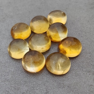 May include: Nine round, smooth, translucent yellow gemstones. The gemstones are arranged in a cluster on a grey surface.