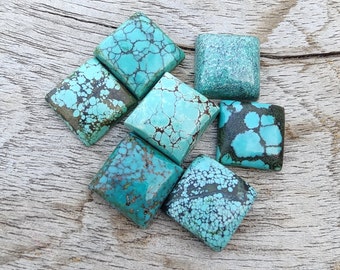 May include: Six square-shaped turquoise cabochons with a blue-green color and brown matrix. The stones are arranged in a cluster on a wooden surface.