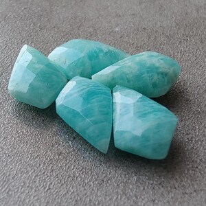 May include: Five faceted, light blue green amazonite gemstones. The stones are irregularly shaped and have a smooth, polished finish.
