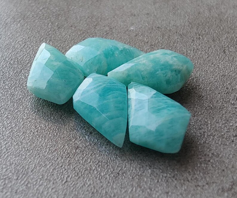 May include: Five faceted, light blue green amazonite gemstones. The stones are irregularly shaped and have a smooth, polished finish.