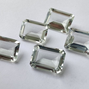 Puede incluir: Cinco piedras preciosas rectangulares transparentes y facetadas con un tono verde claro. Las piedras preciosas están talladas en forma de esmeralda.